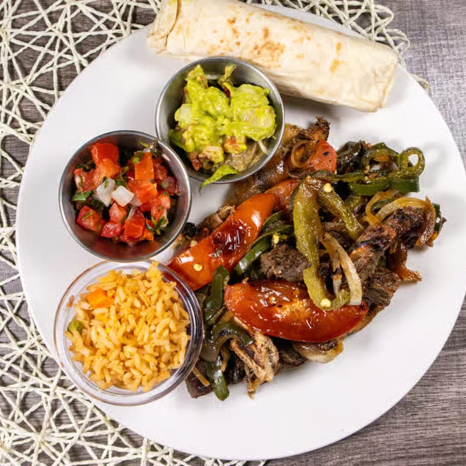 Mexican fajita plate with steak, peppers, onions, rice, guacamole, pico de gallo, and a tortilla.