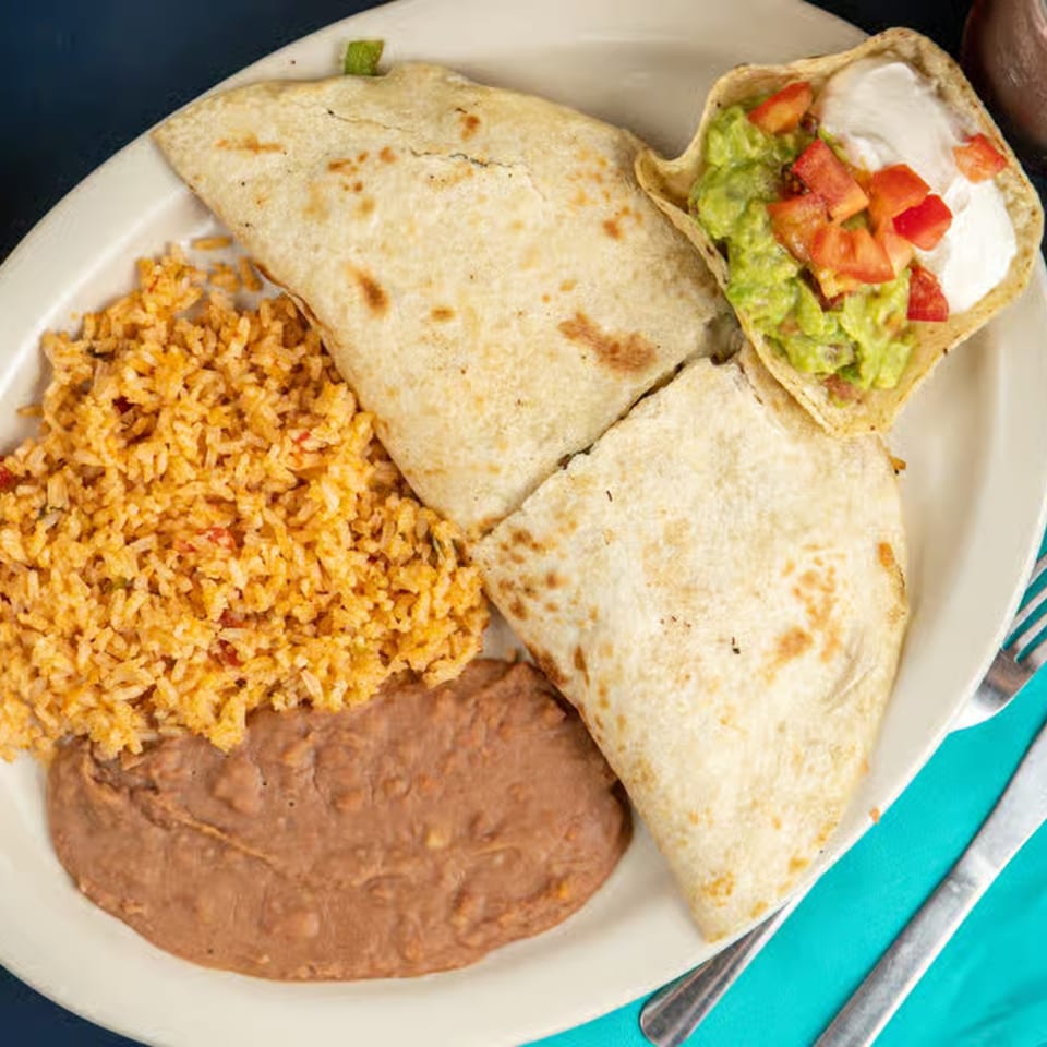 A plate of Mexican food with quesadillas, rice, refried beans, guacamole, sour cream, and diced tomatoes.