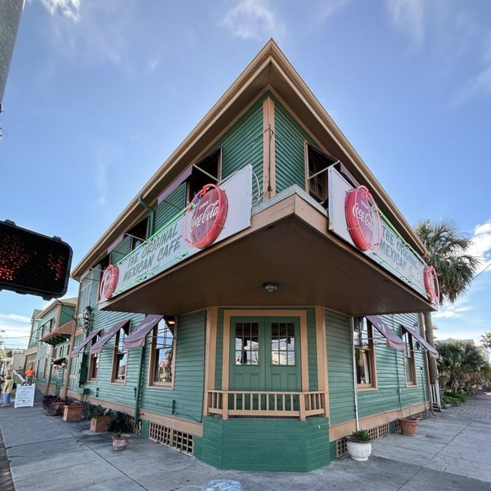 The Original Mexican Cafe, a green and tan corner building with Coca-Cola signs, under a blue sky.