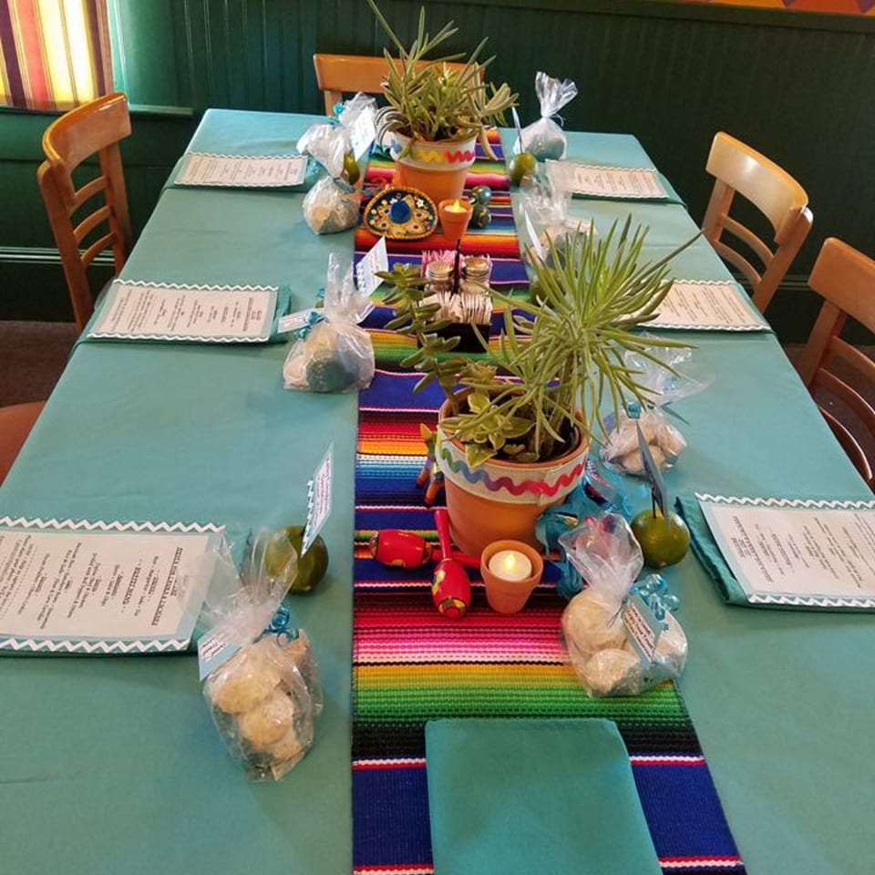 A long table set with a teal tablecloth, colorful Mexican runner, potted succulents, and party favors.