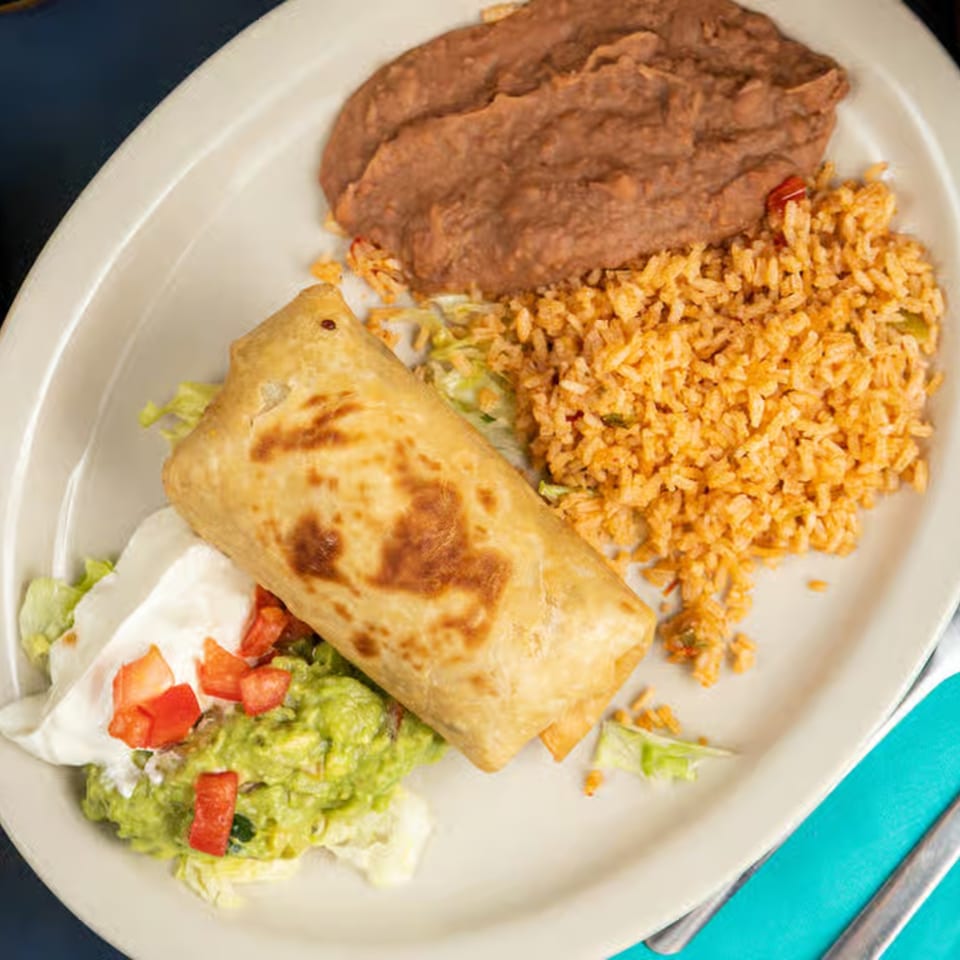 A golden-brown chimichanga with refried beans, rice, guacamole, sour cream, and diced tomatoes.