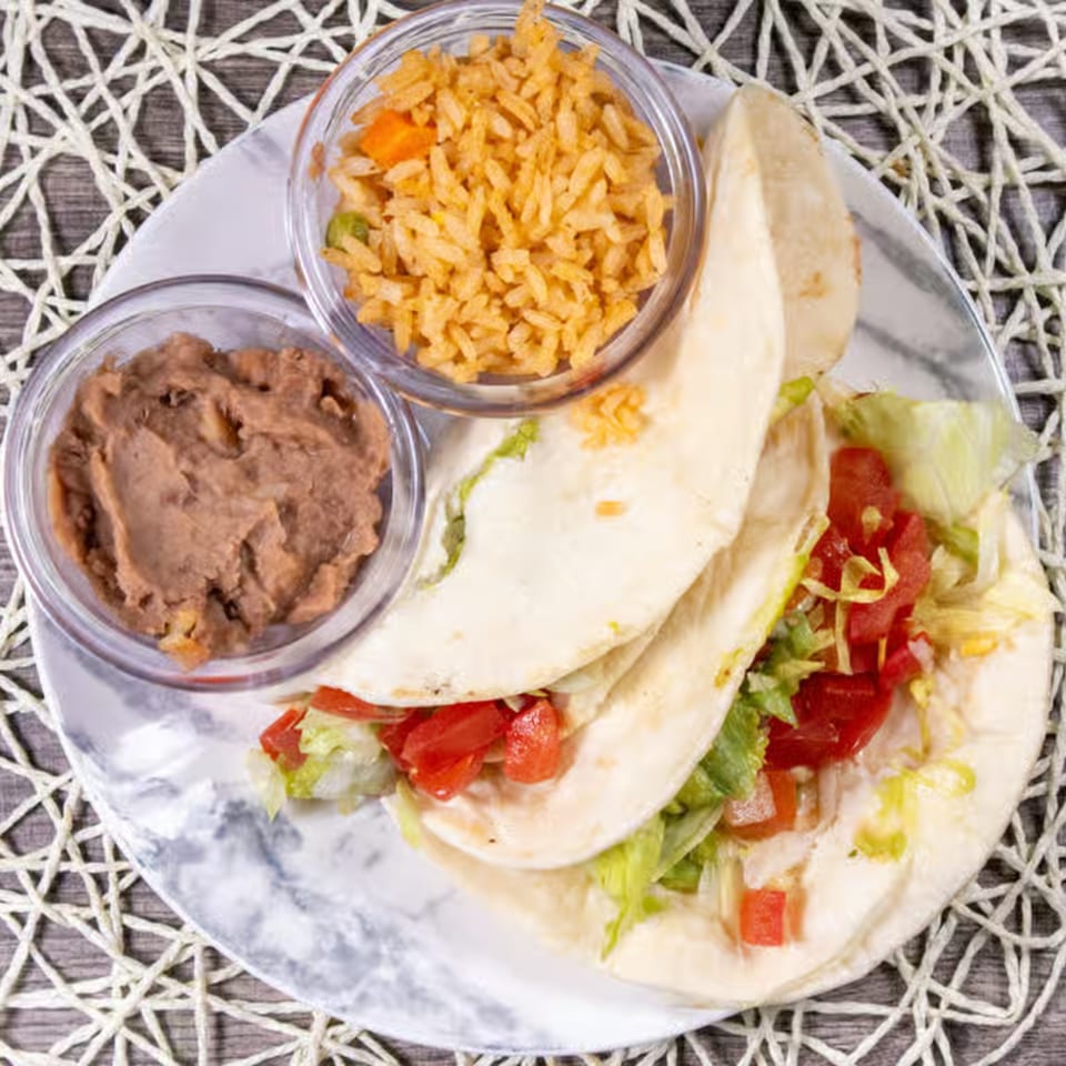 Two soft tacos with lettuce and tomatoes, served with sides of refried beans and Mexican rice.