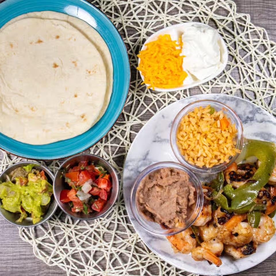 Shrimp fajitas with grilled peppers, rice, refried beans, guacamole, pico de gallo, and tortillas.